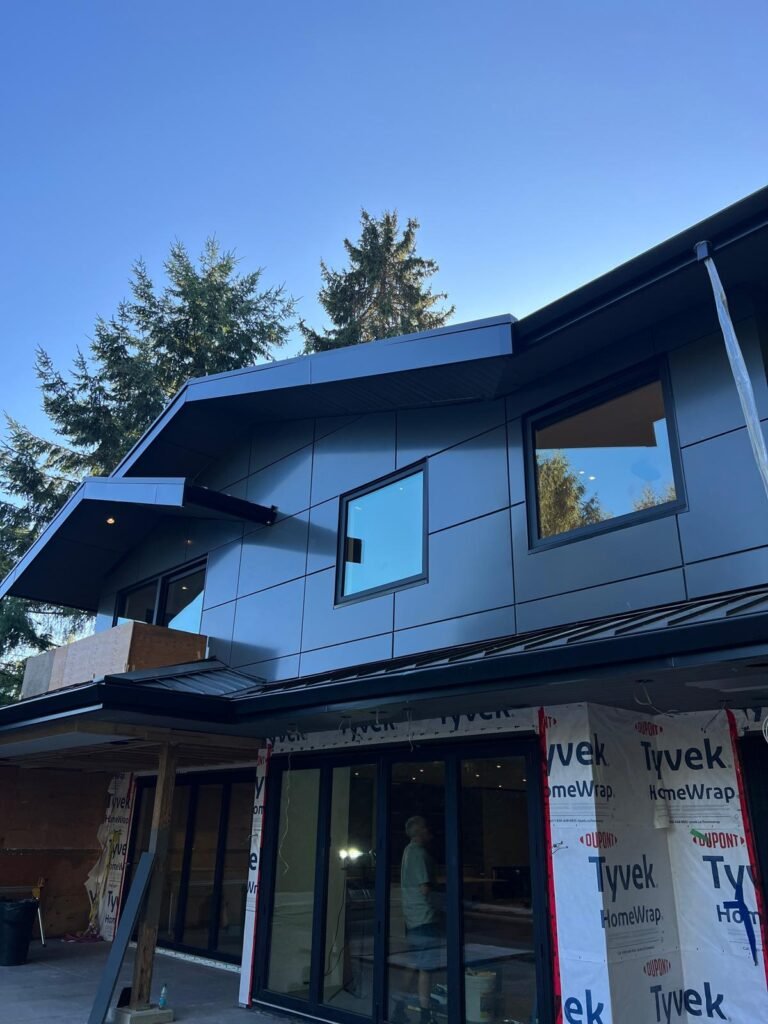 Building exterior mid-installation showing ACM panel siding completed on one section while the Tyvek air barrier remains exposed on the adjacent wall
